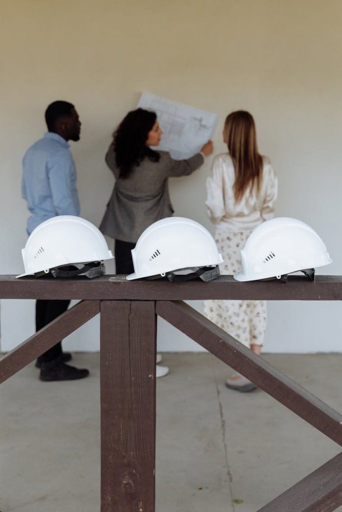 man-and-women-looking-at-house-floor-plan-8469988 Group of architects discussing construction plans with hard hats in focus.